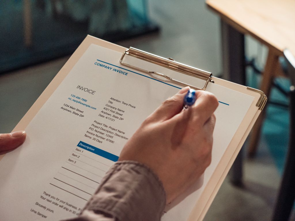 Contact Us Person's hand holding a company invoice on a clipboard with a pen.